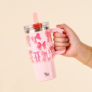 Pink tumbler with bow pattern held by a hand against a beige background