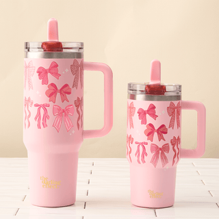 Two pink tumblers with bow patterns on a light wooden surface.