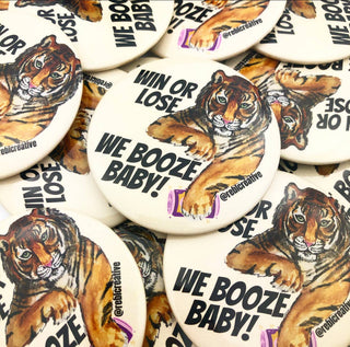 Buttons with tiger design and 'We Booze Baby!' text on a pile.