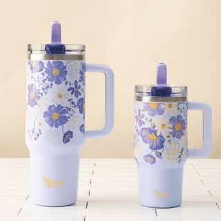 Two floral-patterned tumblers with handles on a light wooden surface.