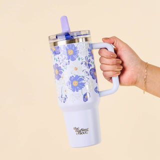 Hand holding a floral-patterned tumbler with a straw on a beige background