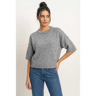 A woman wearing a heather gray short-sleeve knit sweater and blue jeans, standing against a plain light background.