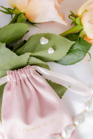 Pink jewelry pouch with 'LINNY CO' branding on a white background with green leaves and peach flowers.