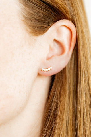 Close-up of an ear wearing a gold earring with a plain background