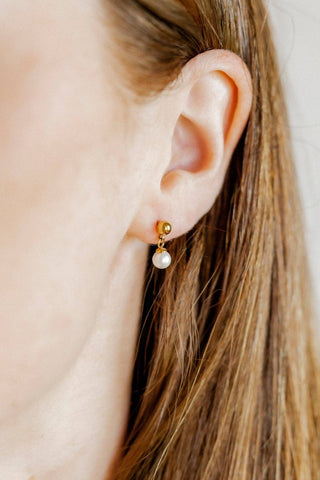 Close-up of an ear wearing a gold earring with a pearl drop.