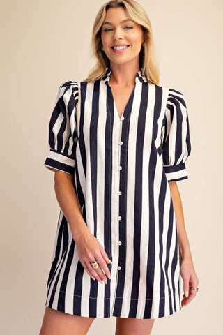 A woman modeling a short puff-sleeve shirt dress with vertical navy and white stripes, featuring a button-down front and collar, set against a solid beige background.