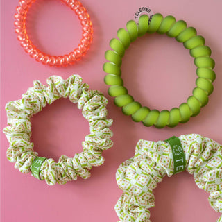 Three hair ties and scrunchies on a pink background with 'Fleeties' branding.