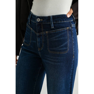 Close-up of a person wearing dark blue denim jeans with a light gray top and black jacket, showing the back pocket and waistband details.