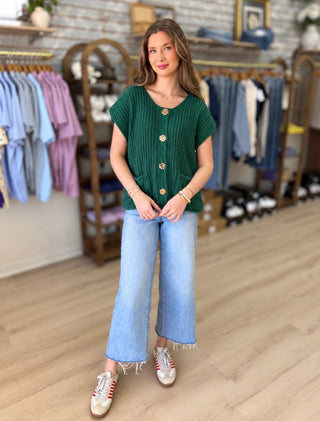 Model wearing forest sweater with gold buttons and jeans in clothing store