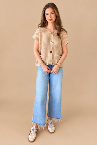 Model wearing a taupe cap sleeve chunky sweater with gold buttons on tan background