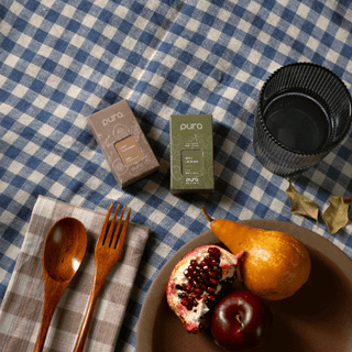 Table setting with pomegranate, pear, plums, wooden spoon and fork on a checkered tablecloth.
