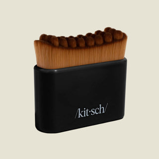 A black rectangular brush holder with the KitSch logo, holding a row of thick brown bristle makeup brushes, photographed on a light gray background.