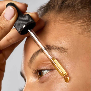 Person applying a dropper of liquid to their eye with a neutral background