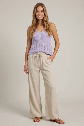 Woman wearing a light purple sleeveless top and beige pants on a plain background