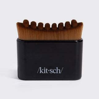 A Kit-Sch grooming brush with brown bristles and a black handle, featuring the Kit-Sch logo on the front, set against a plain light gray background.