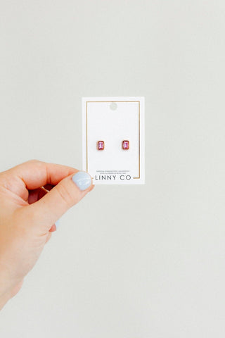Hand holding a card with pink earrings on a light gray background