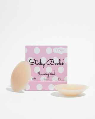 A pink polka-dot box labeled 'Sticky Boobs the original' with two pale peach adhesive pads placed in front on a clean white background.