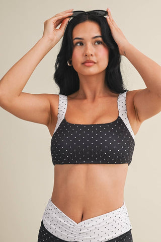 Woman wearing a black and white polka dot sports bra and leggings on a beige background