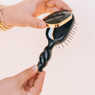 Black hairbrush with gold accents held by a hand against a light background