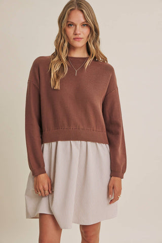 A woman modeling a brown cropped knit sweater with a pleated light beige skirt, photographed against a plain warm beige studio background.