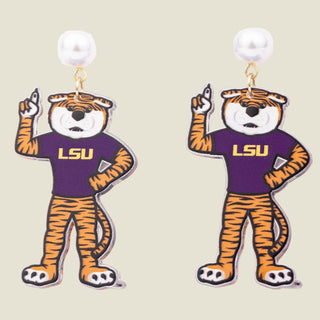 A pair of dangling earrings featuring a cartoon LSU tiger mascot wearing a purple shirt with gold 'LSU' lettering, with a white pearl stud at the top and gold hooks, shown on a plain white background.