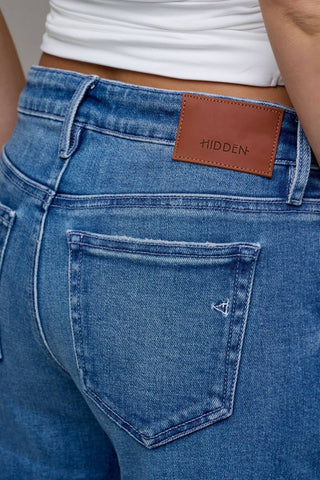 Close-up of blue jeans with a brown leather patch and 'HIDDEN' branding.