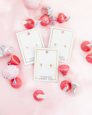 LINNY CO earrings on display with decorative pink and red items on a pink background