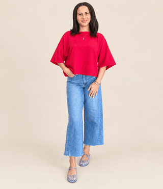 A woman modeling a bright red short-sleeve top and light blue wide-leg jeans against a solid beige studio background.