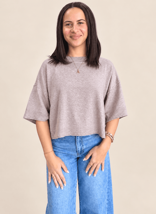Model in tan short sleeve sweater, jeans and a tan background