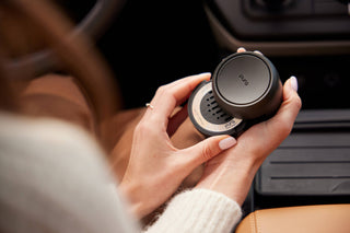 Person holding a black car cup holder with a brand logo inside a vehicle.