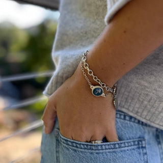 Person wearing a silver bracelet with a blue stone on a blurred outdoor background