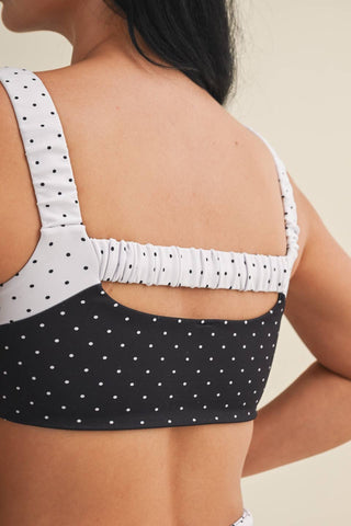Black polka dot sports bra with white ruched straps on a neutral background