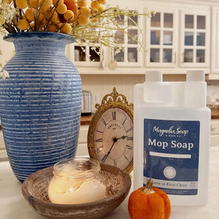 Mop soap bottle with decorative items including a blue vase, candle, and small pumpkin on a kitchen counter.