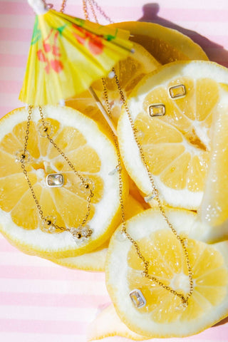 Necklace with a diamond pendant on lemon slices against a pink background