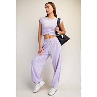 Woman wearing a matching lavender outfit with a black bag on a plain background
