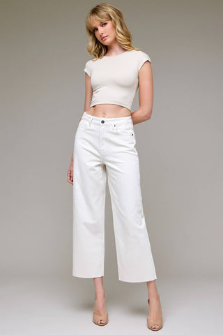Woman wearing a white top and white pants against a plain background