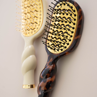 Two hairbrushes, one with a tortoiseshell handle and the other with a white handle, on a light background.