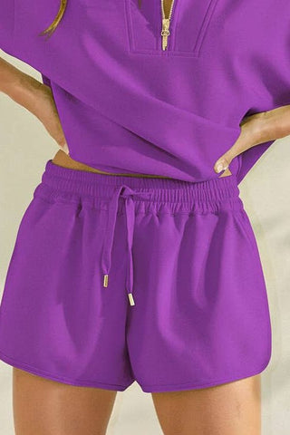 Person wearing a purple outfit with shorts and a top on a beige background