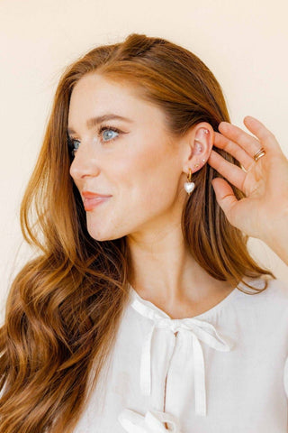 Woman adjusting an earring with a plain background
