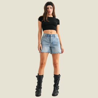 Woman wearing a black crop top, denim shorts, and black knee-high boots on a white background