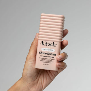 Hand holding a bottle of 'kitsch' Shine Serum against a gray background