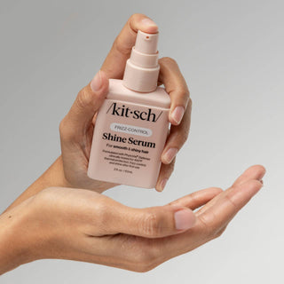 Hand holding a bottle of Kitsch Shine Serum against a gray background