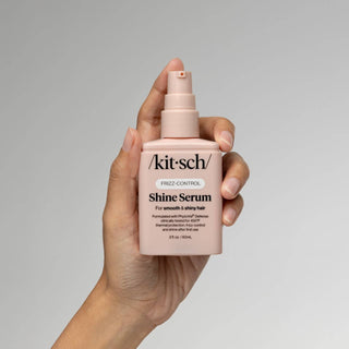 Kitsch shine serum with a handholding it on a light grey background.