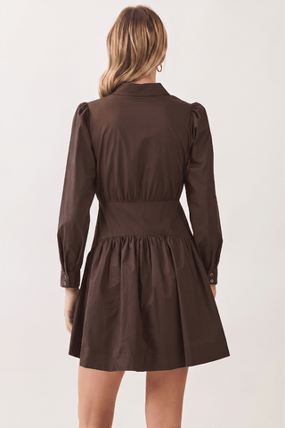 A woman viewed from the back wearing a dark brown long-sleeve mini dress with puffed shoulders and a gathered waist, against a plain light background.