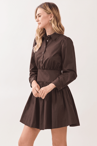 A woman modeling a dark brown long-sleeve mini dress with a button-down collar, gathered waist, and flared skirt against a plain light background.