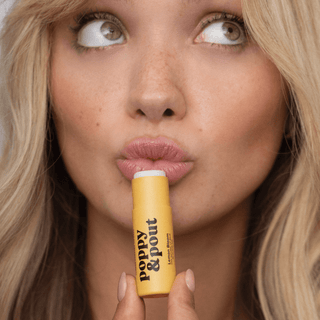 Woman holding a yellow lip balm with 'Poppy & Pout' branding.