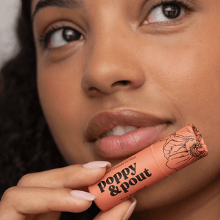 Close-up of a person holding a 'Poppy & Pout' product near their lips.