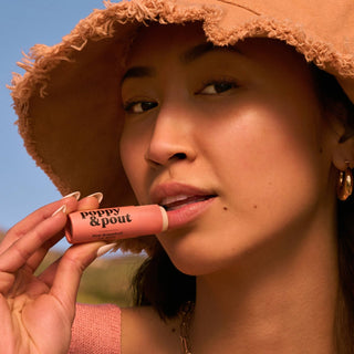 Woman applying Poppy & Pout lipstick with a straw hat on a sunny day