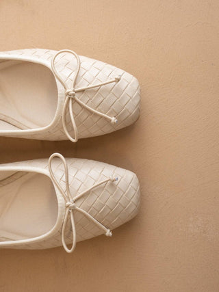 Pair of white quilted shoes with bow details on a beige background