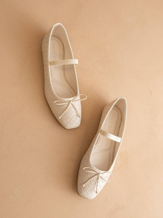 Pair of white ballet flats with a bow on a beige background
